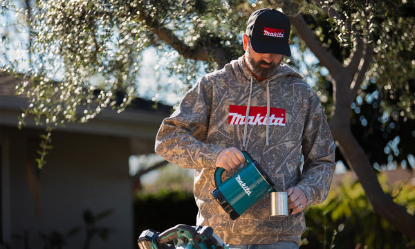 Man wearing a Makita hoodie holding a power tool outdoors.